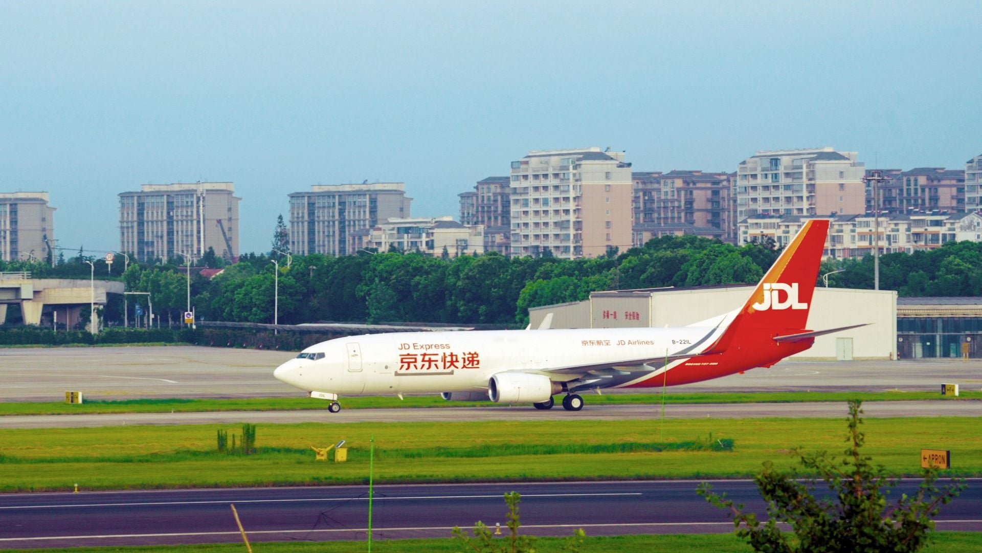 A red-and-white JD Airlines freighter on the taxiway with apartment buildings in the background.