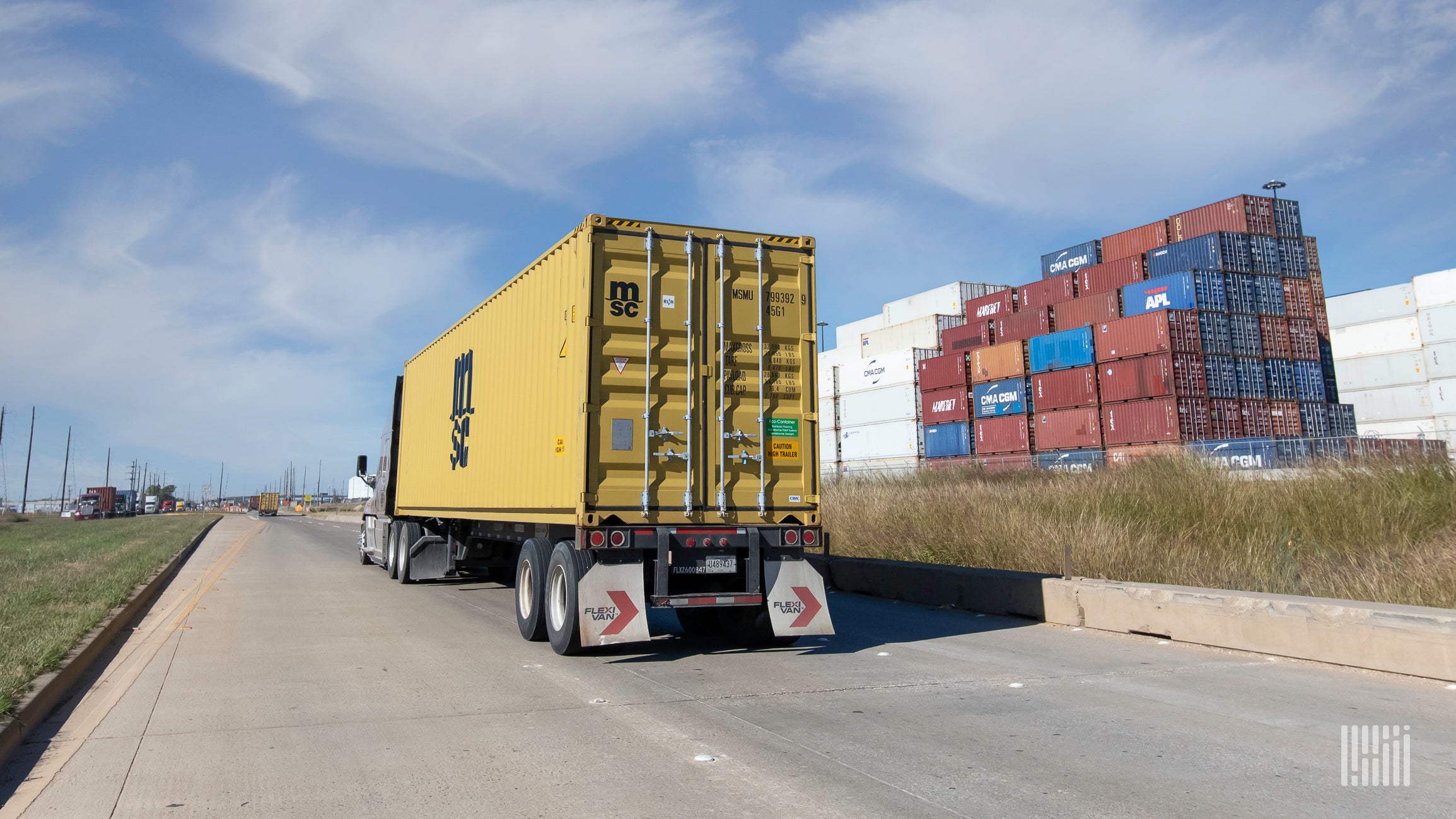 A yellow ocean container being pulled by a truck