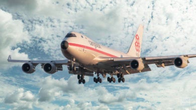 A large, white 747 freighter comes in for landing, heading toward camera with white clouds in the background.