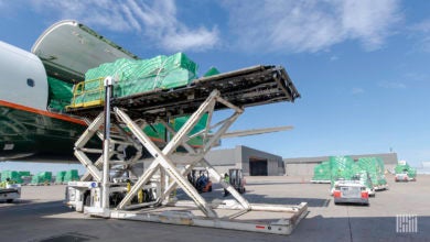 A container on a hydraulic lift being loaded through side door of a plane on a bright day.