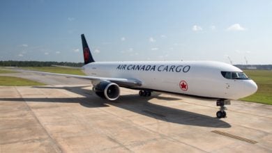 A white Air Canada Cargo jet with black tail and rim on the tarmac on a sunny day.