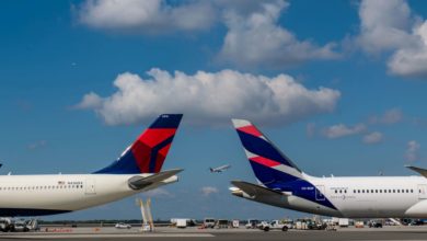 Tail ends of Delta Air Lines and Latam Airlines facing each other on tarmac, with blue sky and white clouds.