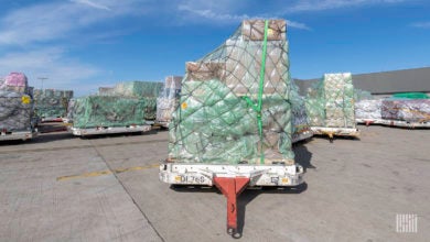 Large pallets with plastic wrapping shipments on airport tarmac on bright day.