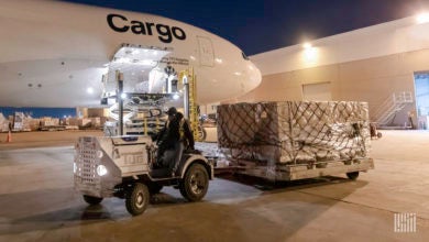 A white jet with Cargo lettering and a tug towing a pallet of freight at night.