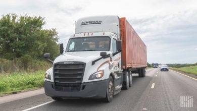 A white Schneider truck pulling a chassis with an orange intermodal container