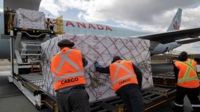 Ground crews with orange vests load a large cargo pallet on a jetliner.