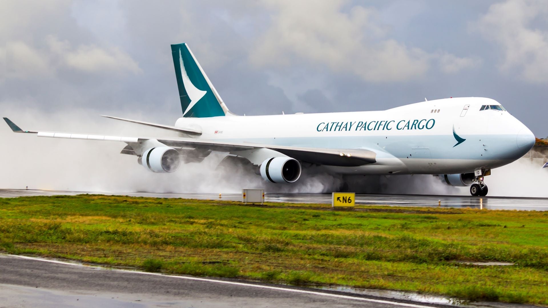 A Cathay Pacific cargo jet sprays water as it lands on a wet runway.