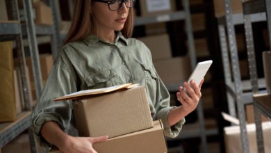 Woman holding phone and boxes in warehouse