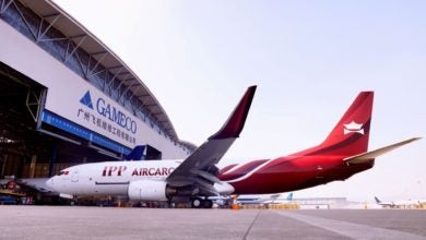 A half white, half red plane in front of a giant hanger.