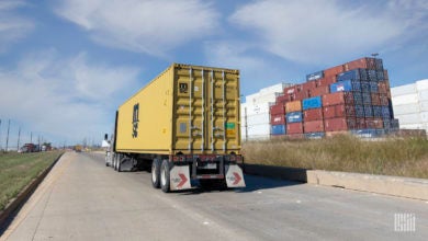 A tractor pulling a chassis with a yellow container at a port