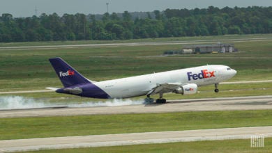 Smoke seen from tires as a white FedEx jet with purple tail lands on runway.