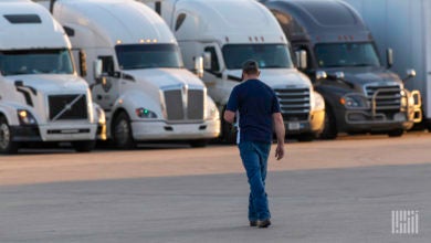 A truck driver walks toward a row of Class 8 tractors in a parking lot.