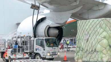 A cargo pallet and a fuel truck under the wing of a large jet.