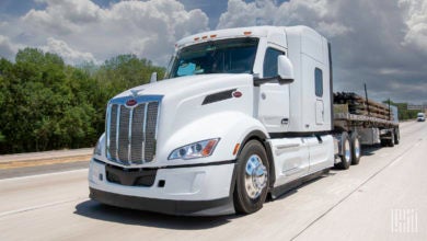 A white tractor pulling a loaded flatbed trailer