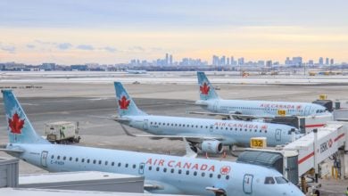 Small Air Canada jets with red maple leaf logos on the tail lined up with city of Toronto in background.