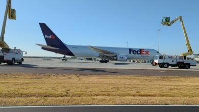 A white FedEx jet with blue tail gets sprayed with de-icing chemicals on a bright day.