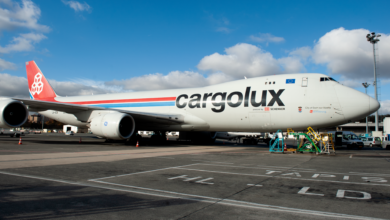 A Cargolux jumbo jet with red tail, side view while parked at airport.