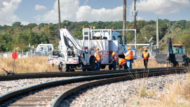 Workers stand next to a machine that is sitting on railroad track.