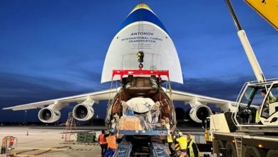 Nose cone of a giant freighter is open to accept an oversize load. Image is at night.