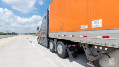 A gray Schneider tractor pulling an orange trailer on the highway