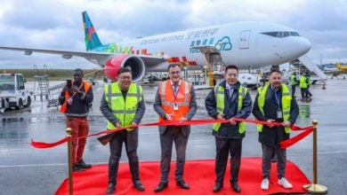 Four men wearing yellow and red safety vests cut a ribbon to welcome a big cargo jet to an airport.