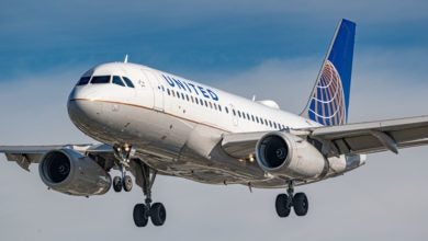 A white United Airlines plane with blue tail with wheels down against a blue sky.