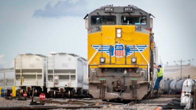 A Union Pacific train is parked in a rail yard next to some hopper rail cars.