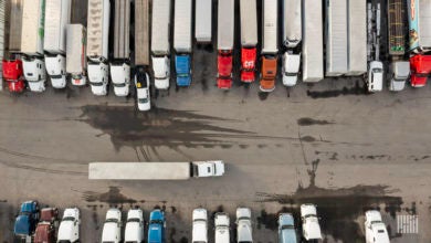 Two rows of tractors sit in a parking lot while one drives in the space between them.