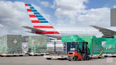 Cargo pallets with green shrink wrap sit by an a jet with an American flag them painted on tail.