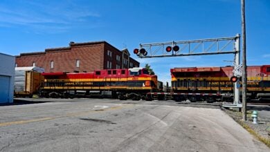 A Kansas City Southern train passes along a grade crossing in the middle of a small town.