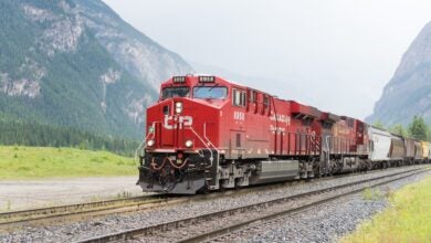 A Canadian Pacific train hauling railcars passes through a valley between mountains.