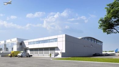 Architectural image of a potential air cargo warehouse at an airport with planes and trucks in the background.