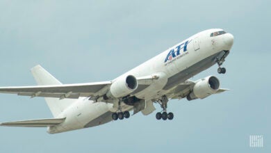 A white jet with ATI logo in the air after takeoff with wheels down.