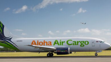 Side view of Aloha Air Cargo jet on a sunny day. Fuselage is white with lime green lettering.