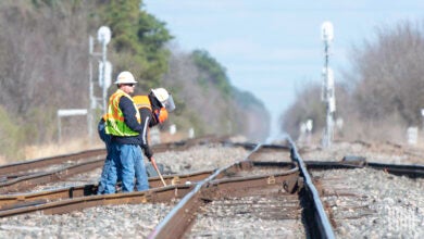 Two men stand by a railroad track and are inspecting it.