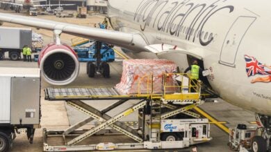 Parallel side view along a Virgin Atlantic jetliner being loaded with freight through the wing door.