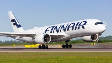 A white jet with blue Finnair lettering touches down on runway on sunny day.