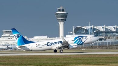 A blue-and-white Egyptair jet lifts off from runway on takeoff on a sunny day.