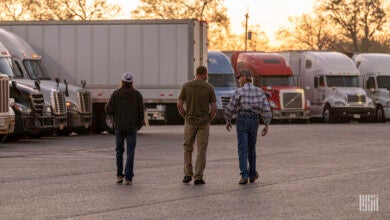 Three people walk in a parking lot toward a row of truck-tractors.