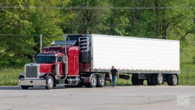 A driver walks along the side of a parked semi truck