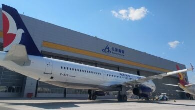 Close up of a passenger jet from the side with a large repair building in the background.