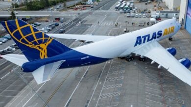 A white jumbo jet with blue-and-gold Atlas Air logo as seen from above outside a hangar.