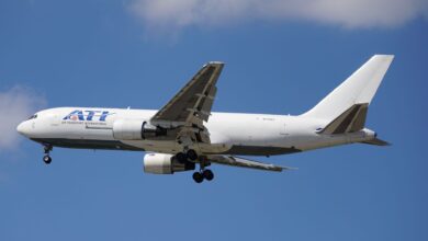 A white cargo jet with ATI lettering seen from below as it flies across blue sky with wheels down.