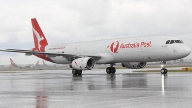 A white plane with red tail and Australia Post label on the side sitting on a tarmac.