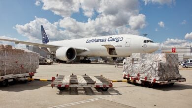 A large Lufthansa Cargo 777 with containers spread on the tarmac waiting to be loaded.