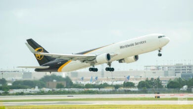 A white UPS jet with a brown tail lifts off the runway on a clear day.