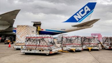 Pallets of cargo on the ramp next to a big freighter with a blue-and-white NCA logo on the tail.