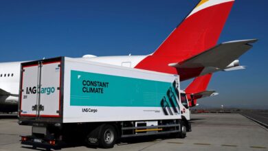 A box van with IAG Cargo lettering and green banner "Constant Climate" on the side in front of a large jet with a red tail.