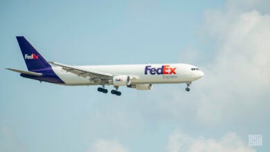 A FedEx cargo jet with a blue tail and wheels down comes in for a landing against a clear sky.