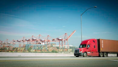 A red truck pulls an ocean container near a port